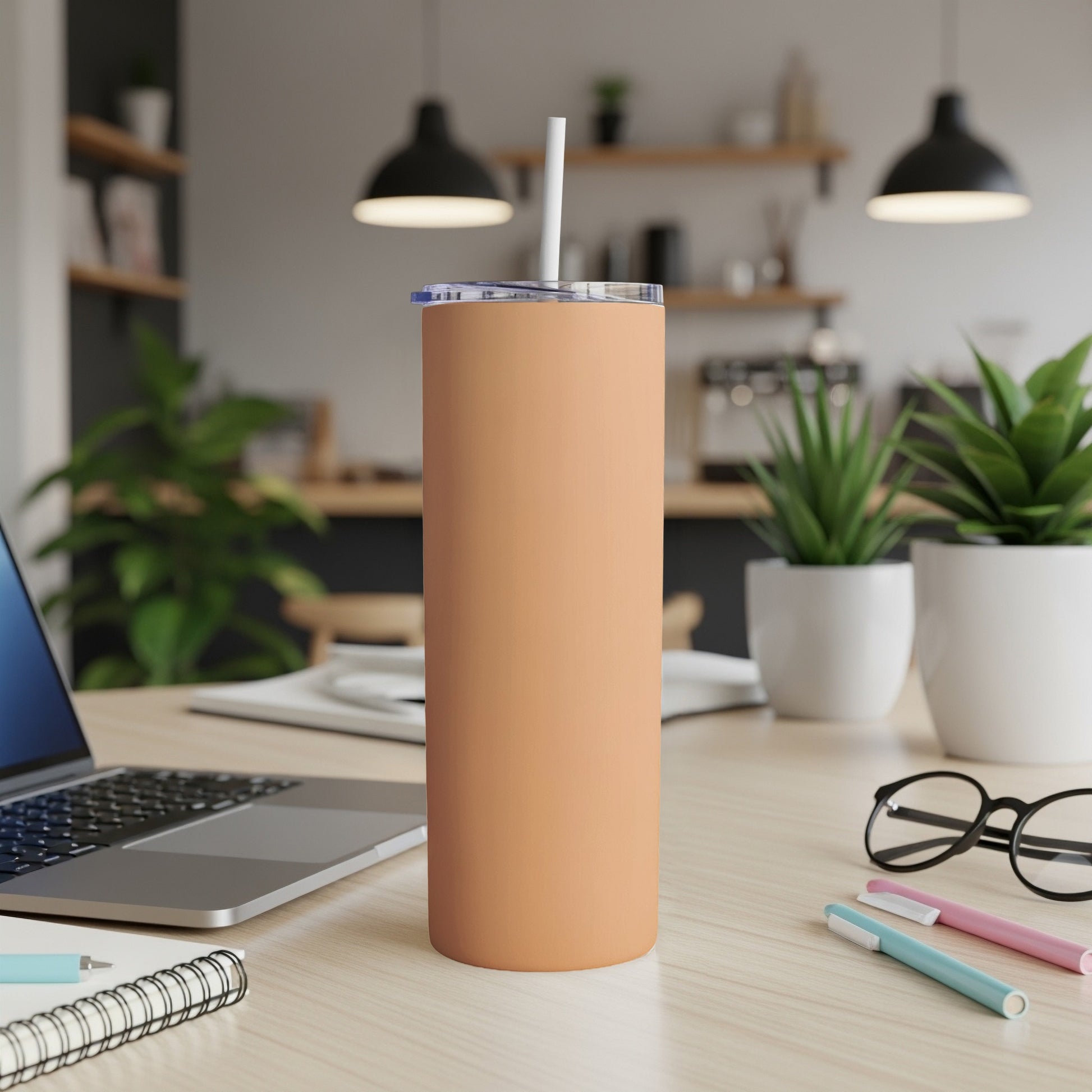 Peach tumbler with straw on a desk with a laptop and pens.
