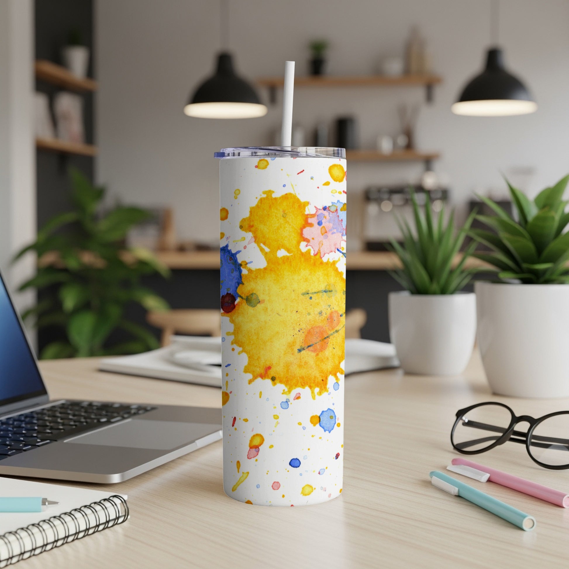 White tumbler with colorful abstract paint splatters and a straw.