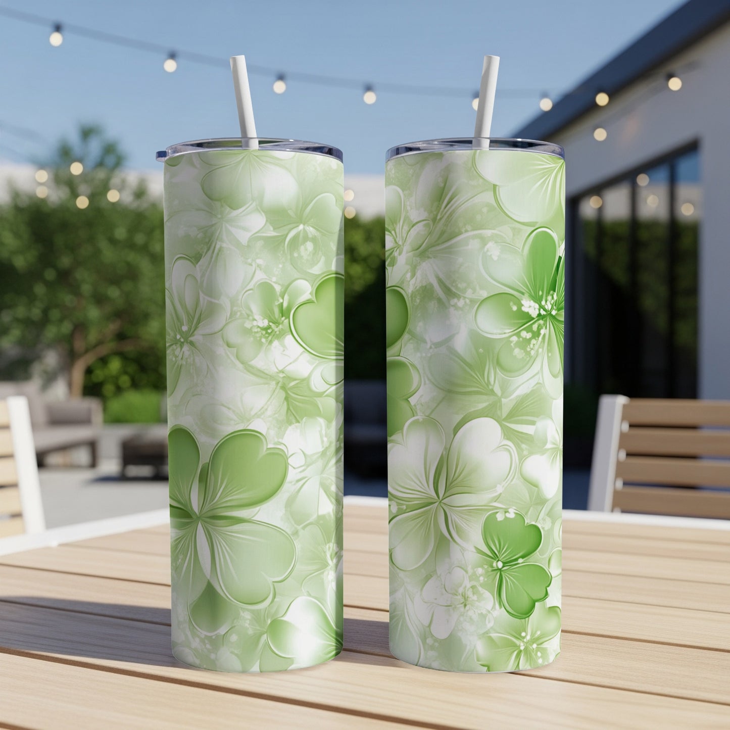 Two green shamrock pattern tumblers with straws on a wooden table outdoors.