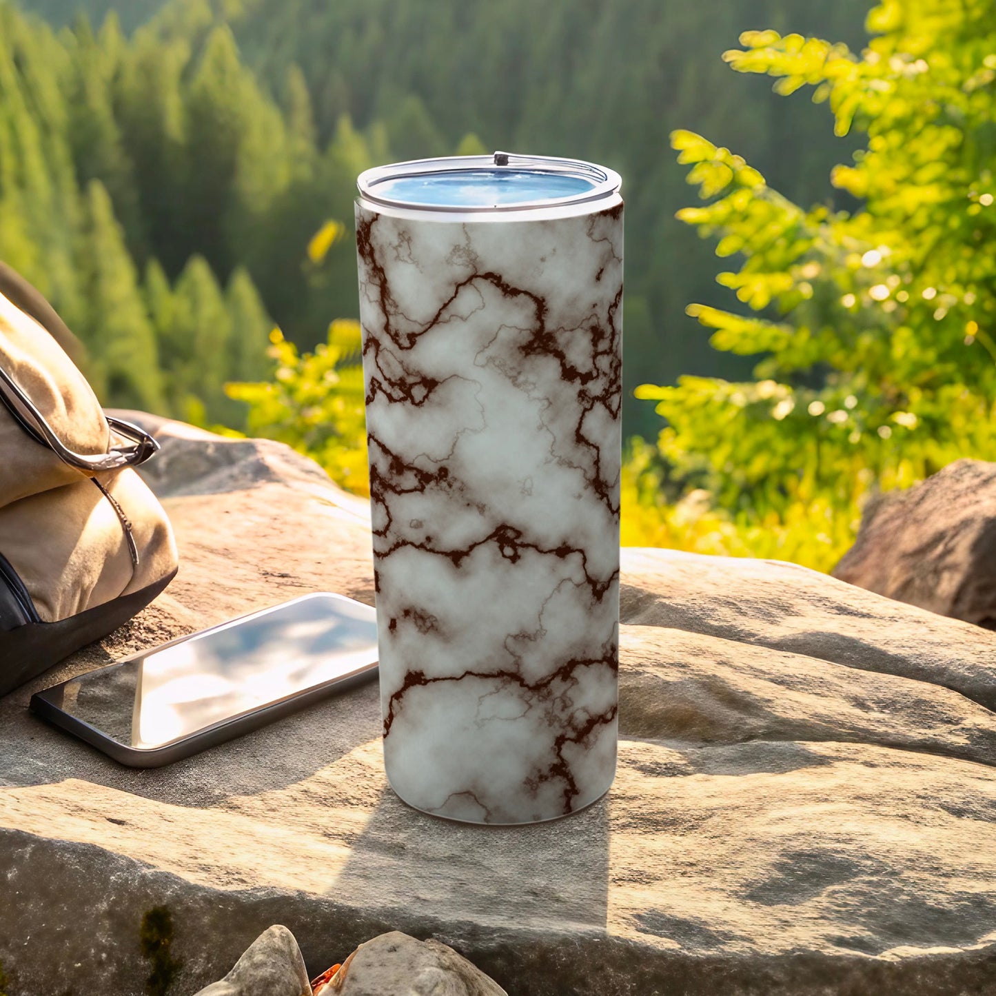 White marble patterned tumbler with smartphone and backpack on rocks.