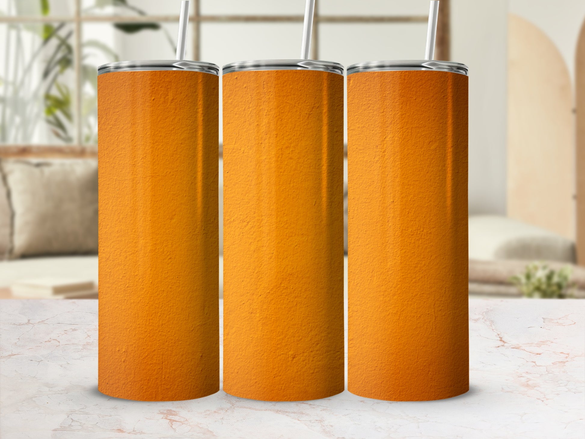 Three orange textured tumblers with straws stand on a marble surface.