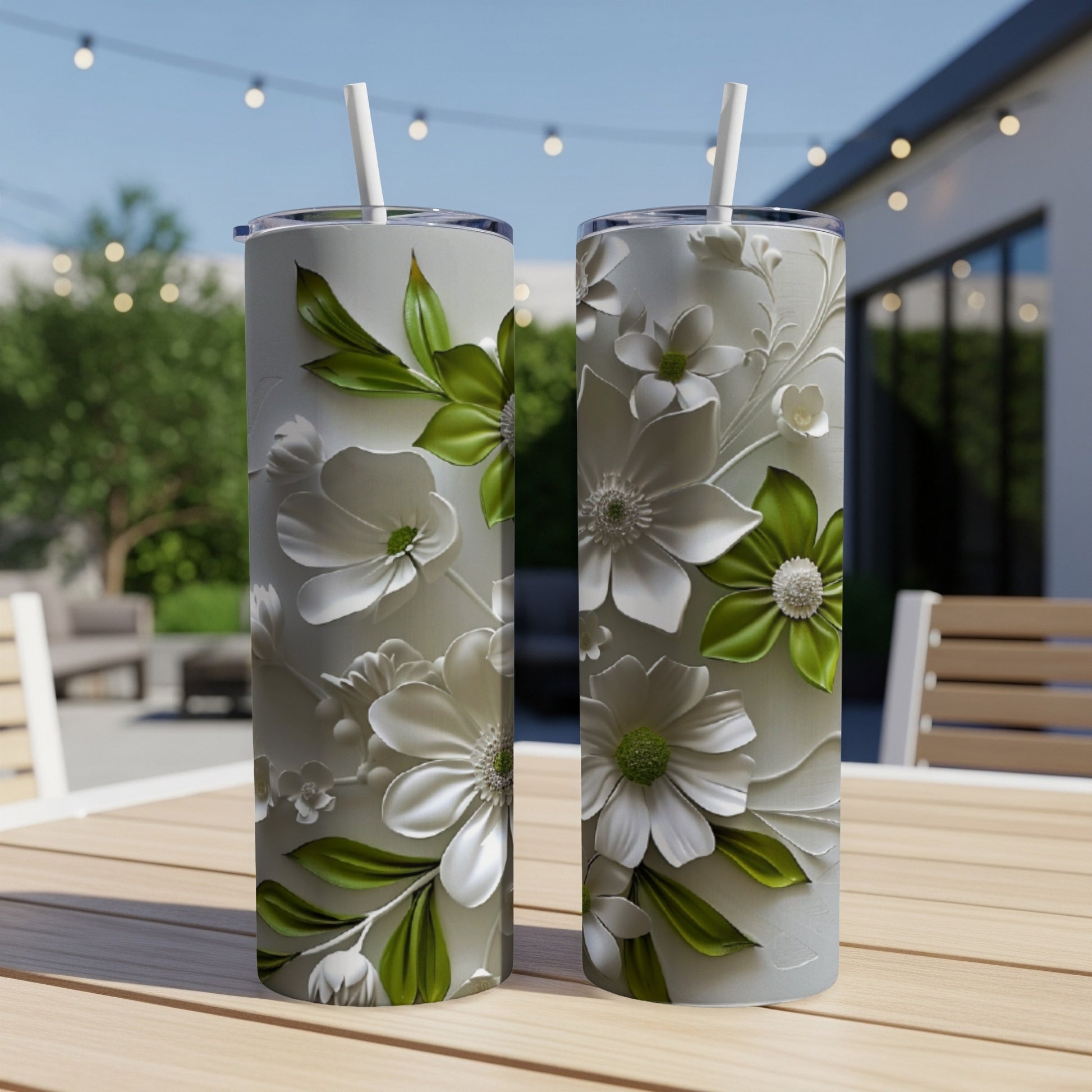 Two white and green floral tumblers with straws on a wooden table.