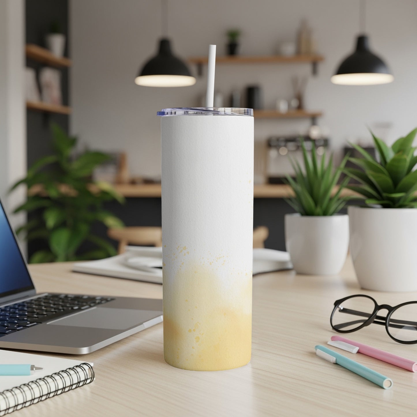 White tumbler with yellow paint splatters, a straw, on a desk.
