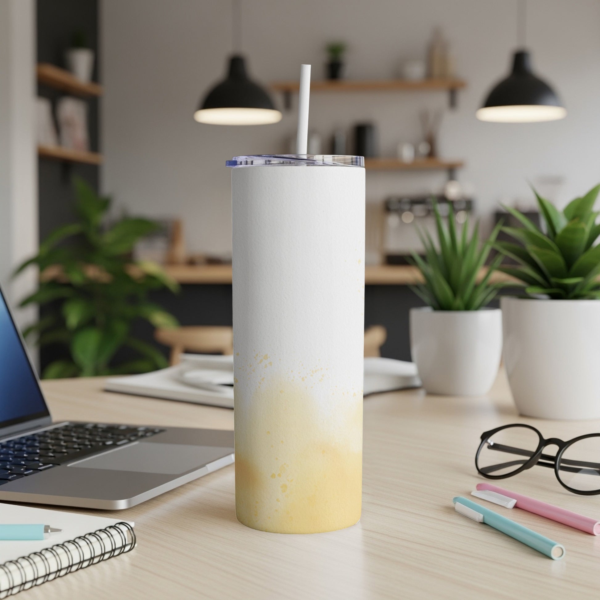 White tumbler with yellow paint splatters, a straw, on a desk.