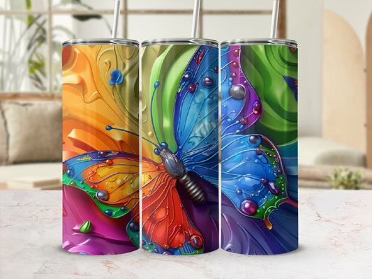 Three colorful, abstract butterfly tumblers with straws displayed on a marble surface.