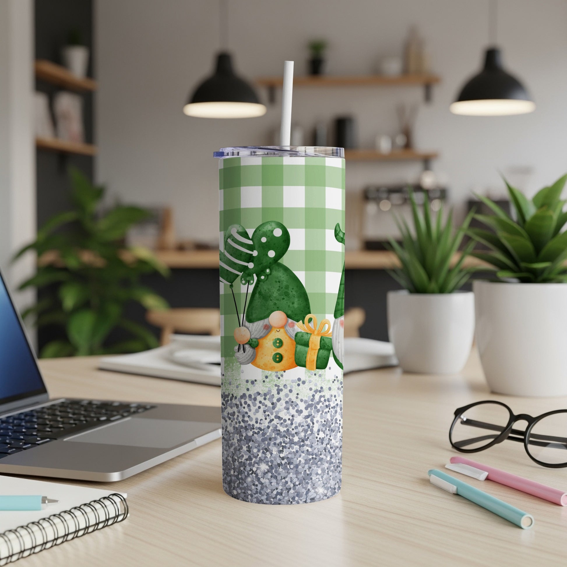 Green plaid tumbler with gnomes, balloons, and glitter on a desk.