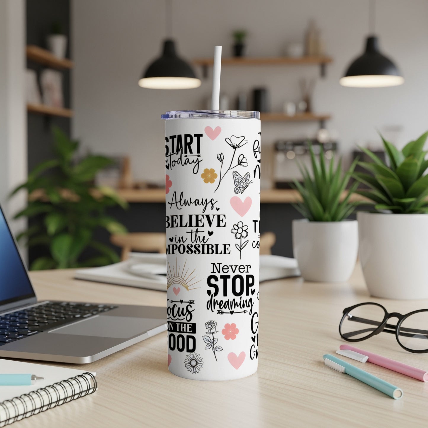 White tumbler with inspirational quotes and floral graphics, on a desk.