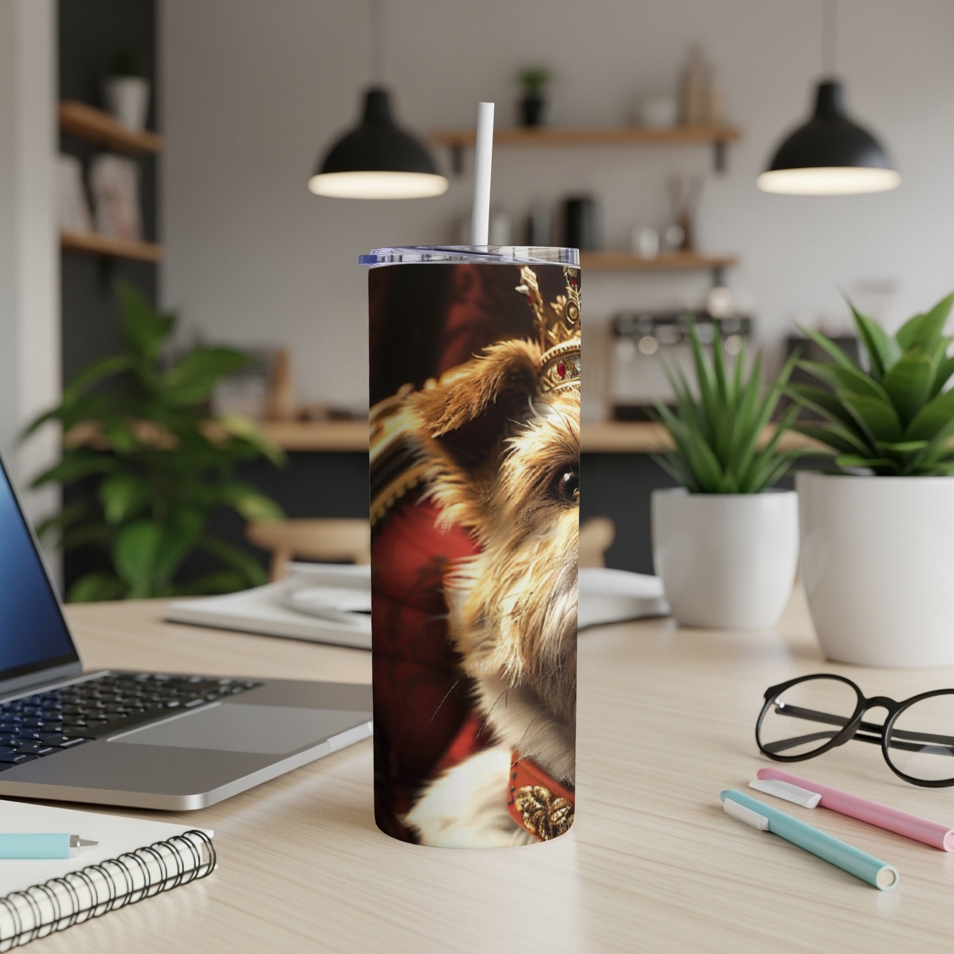 Dog wearing a crown on a tumbler next to a laptop.