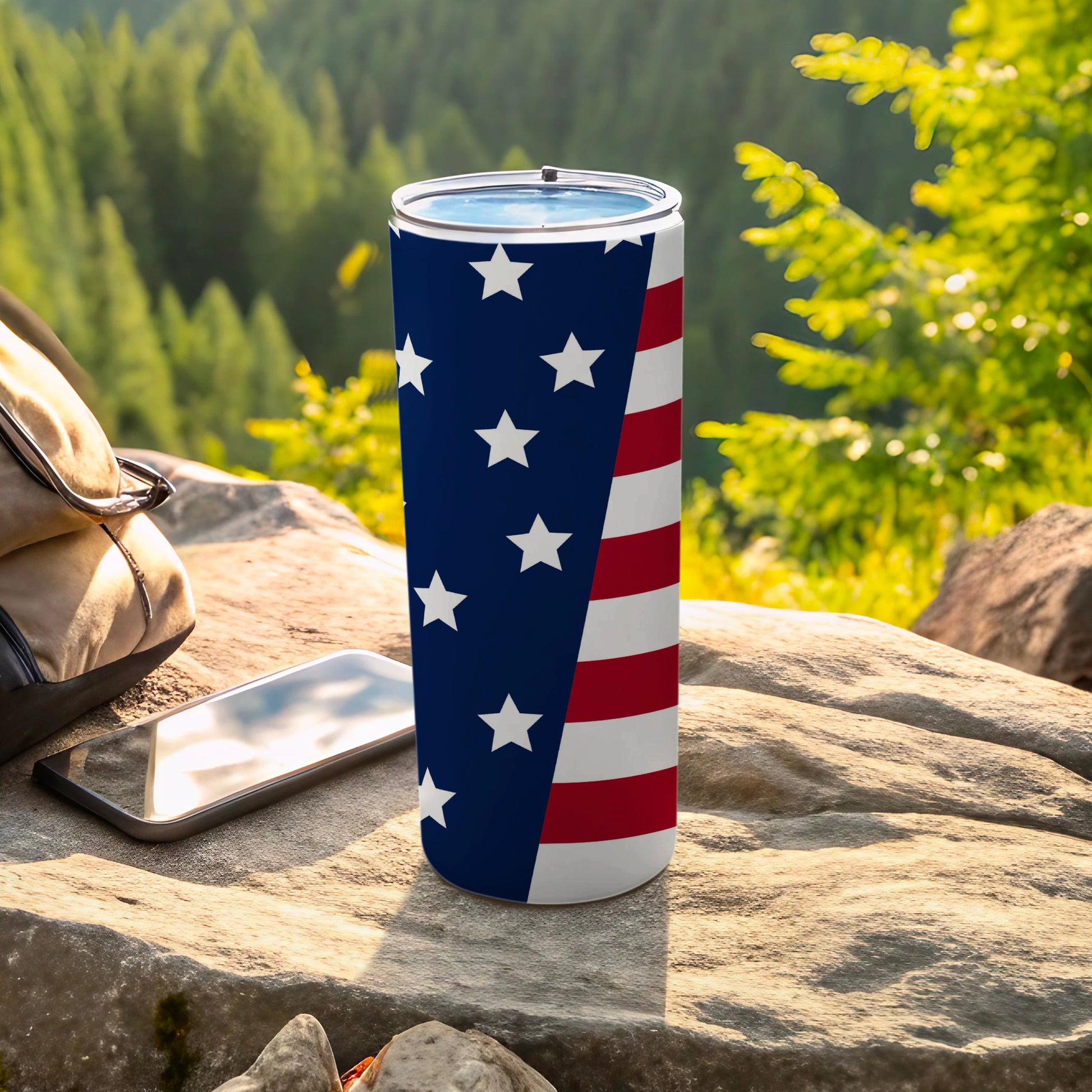 American flag tumbler with a backpack and phone on rocks.