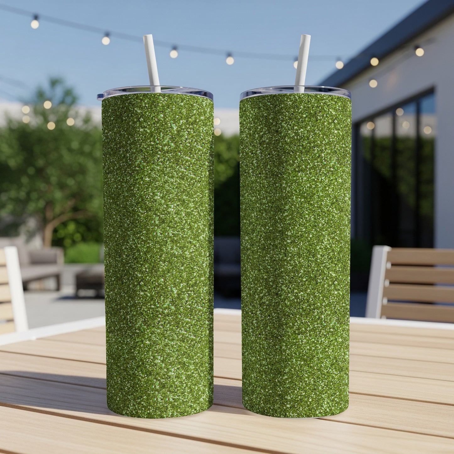 Two tall glittery green tumblers with white straws sit on a wooden table.