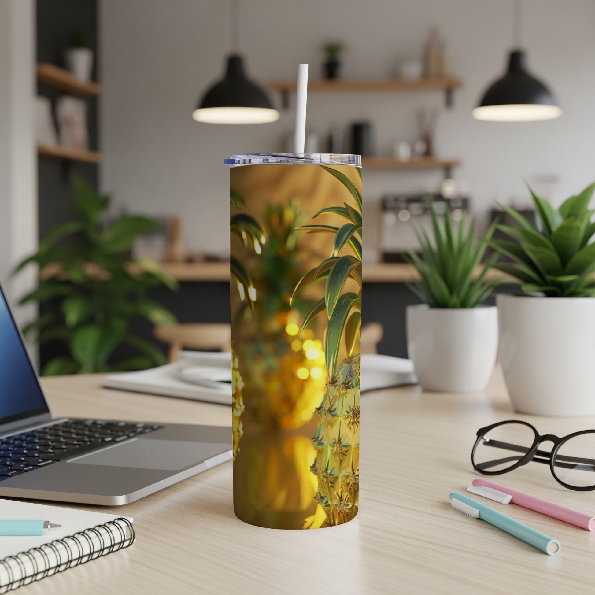 Tall tumbler with pineapple pattern and straw on a desk.