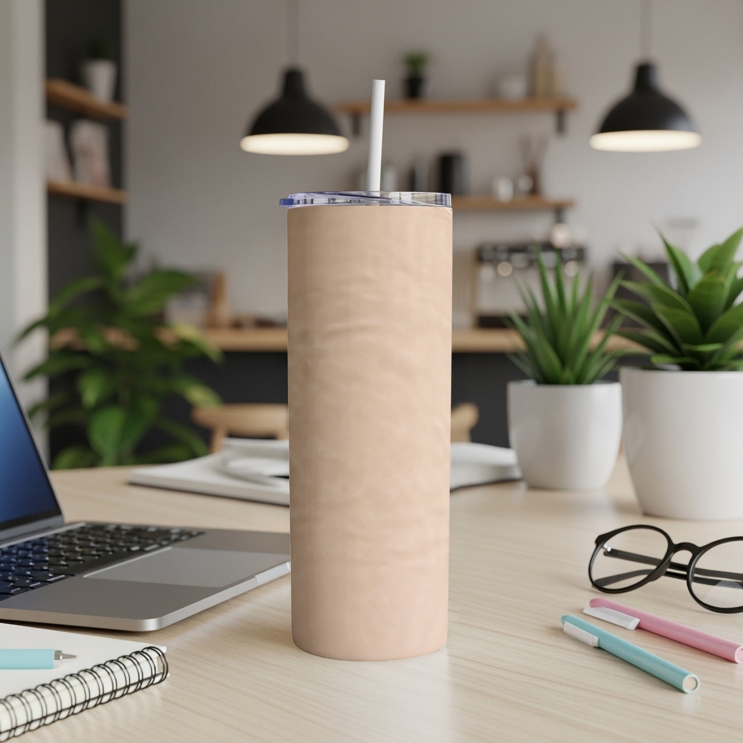 Peach-colored tumbler with straw on a desk next to a laptop.