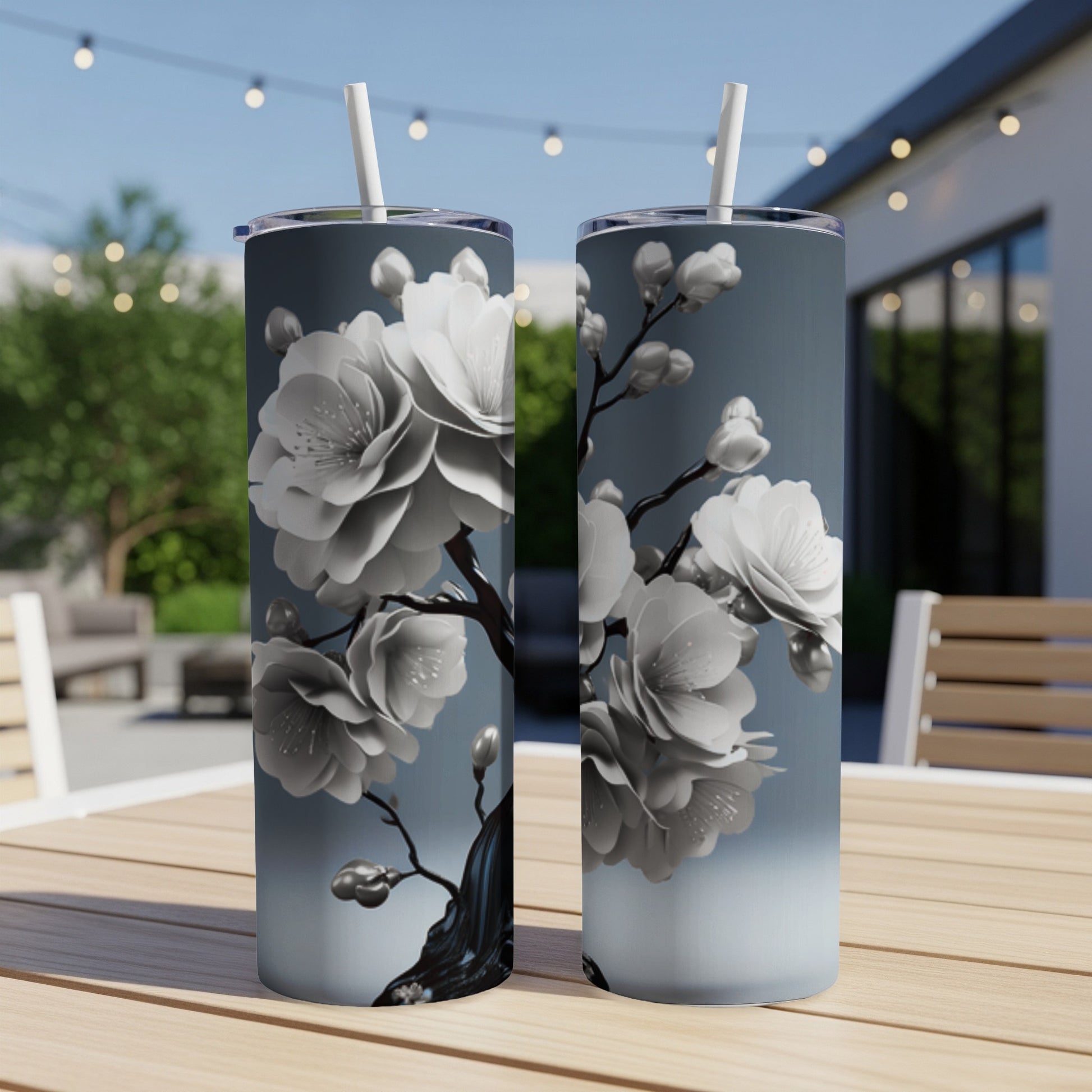 Two gray tumblers with white cherry blossoms against a blurred outdoor patio background.