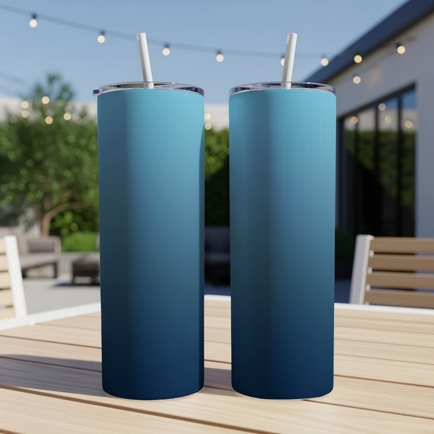 Two gradient blue tumblers with straws sit on a wooden table outdoors.