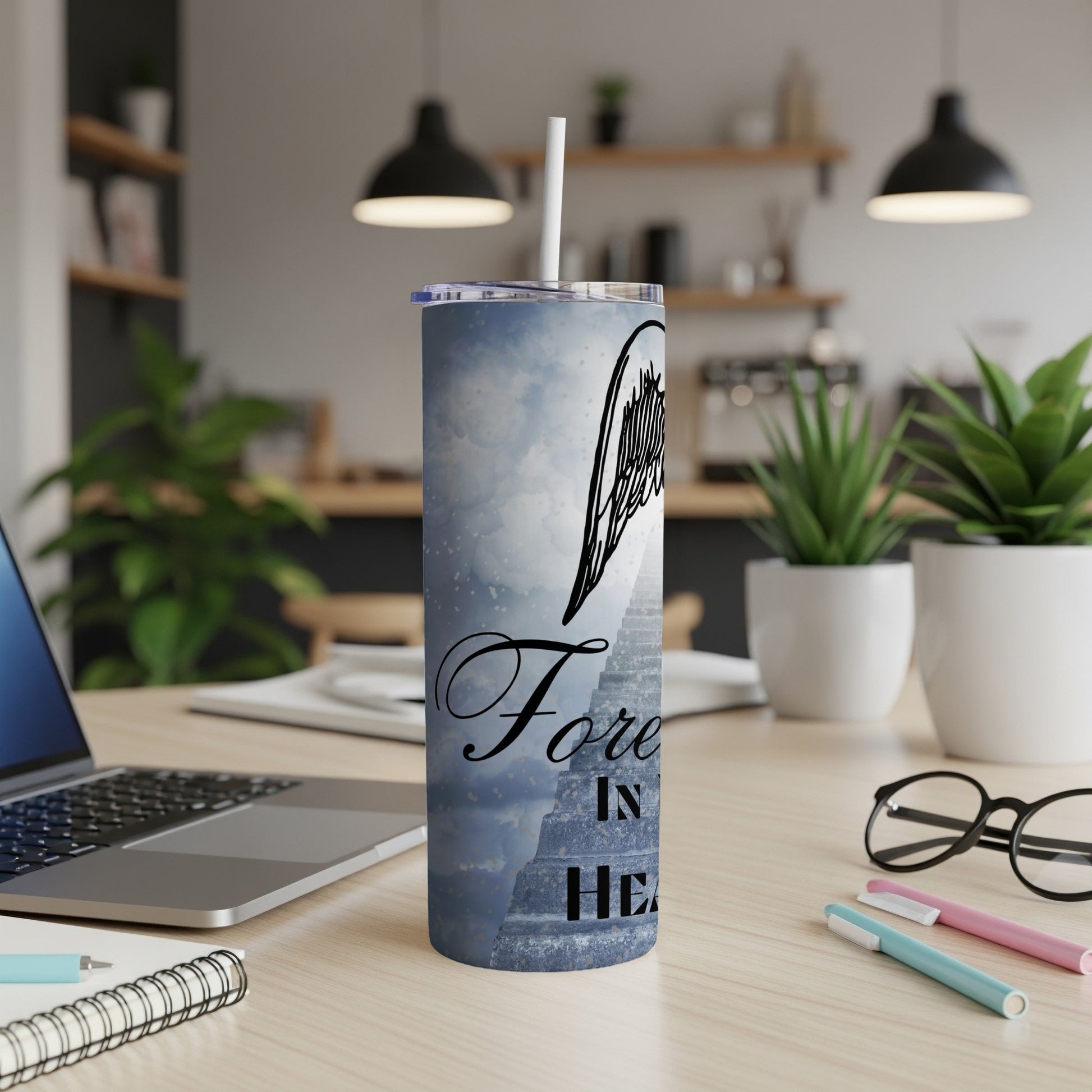 Tumbler with angel wings and text "Forever in Heaven" against a cloudy sky.