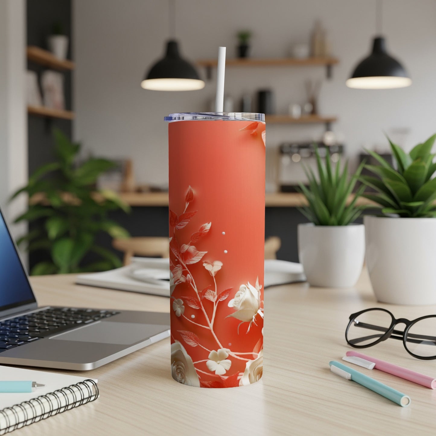 Coral tumbler with white floral pattern and straw on a desk.