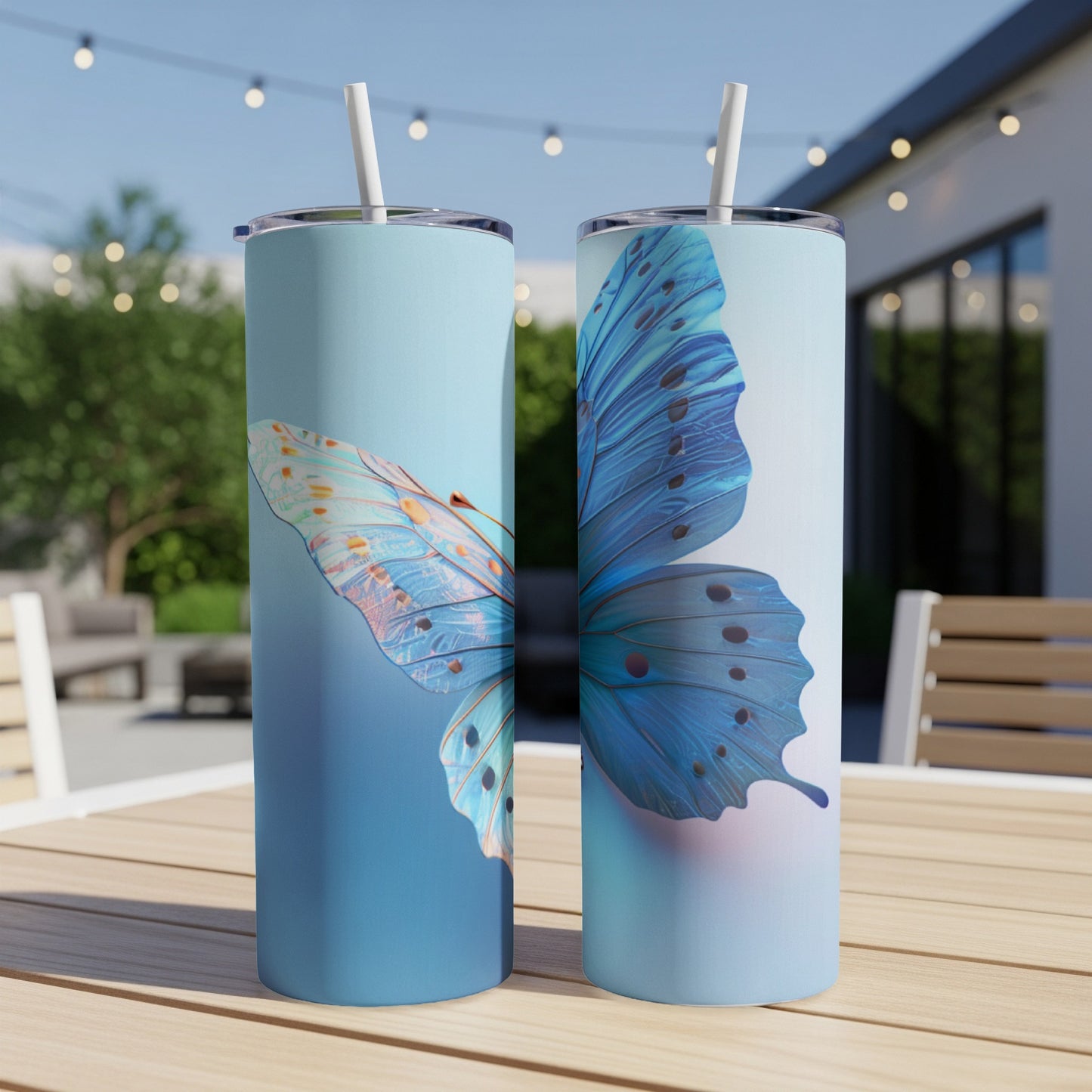Two blue butterfly tumblers with straws on a wooden table outdoors.