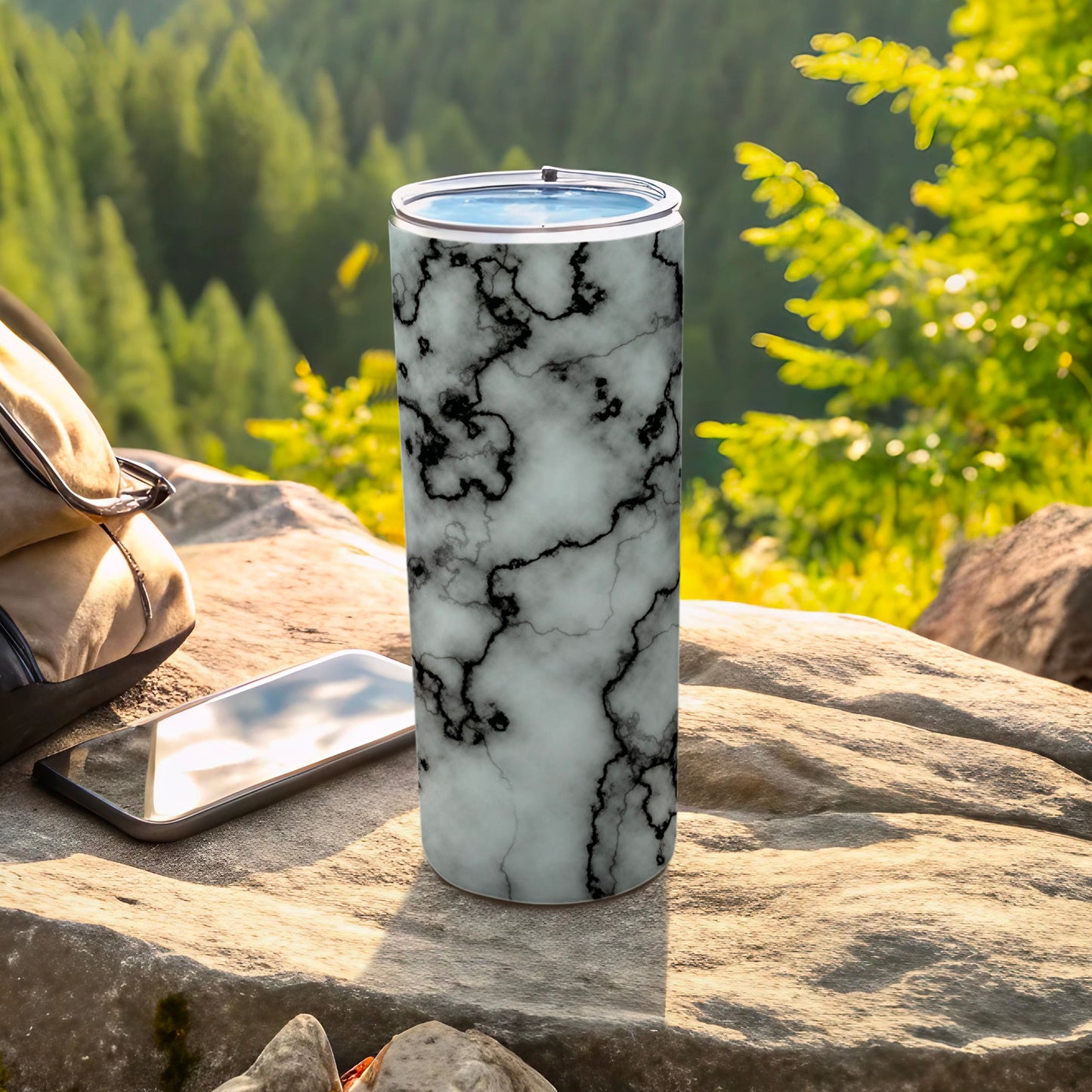 White and black marble tumbler with phone and backpack outdoors.