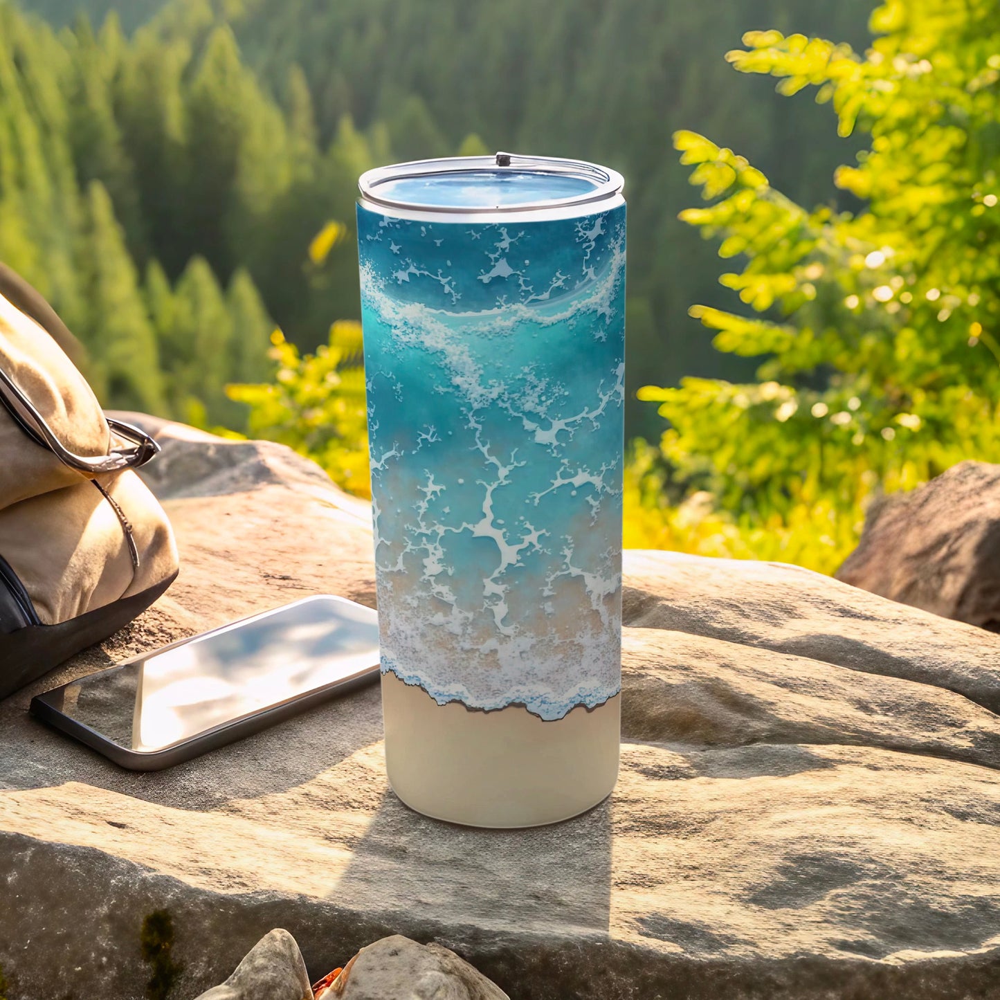 Tall tumbler with ocean wave design, resting on rocks with a backpack and phone.