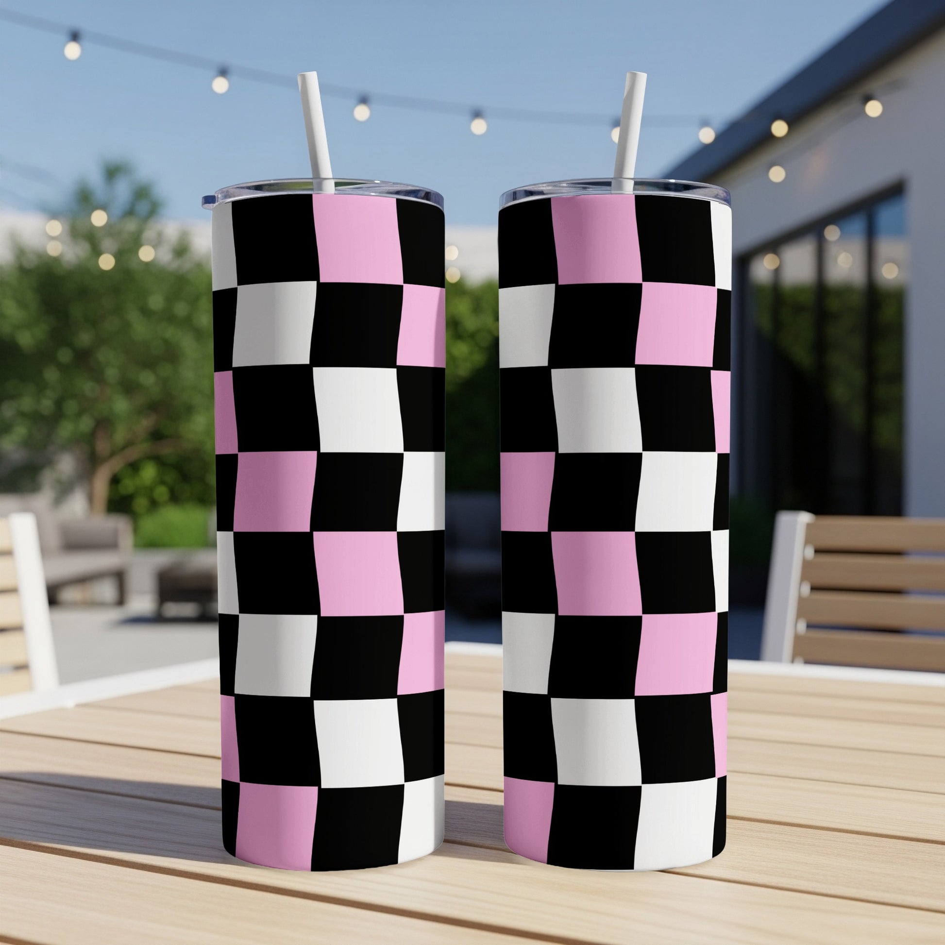 Two pink, black, and white checkered tumblers with straws on a table.