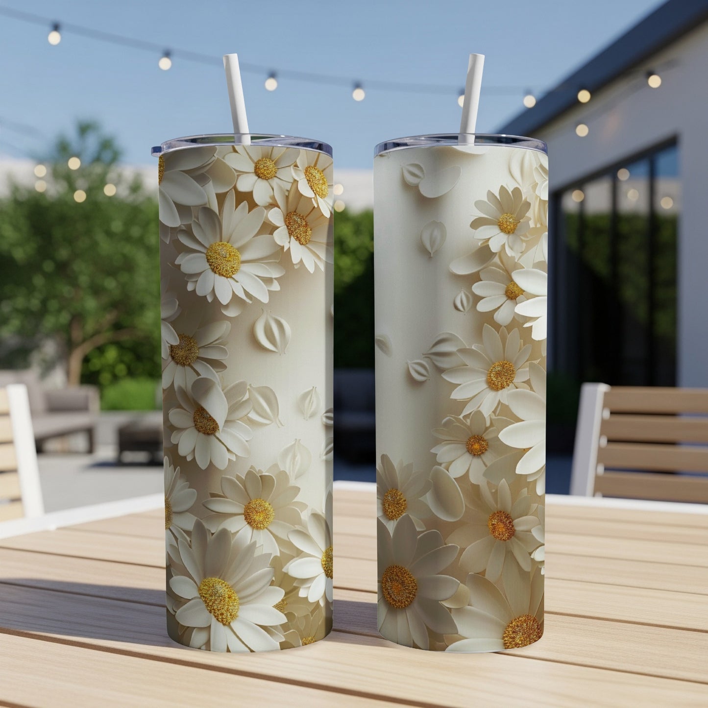 Two white floral tumblers with straws on a wooden table outdoors.