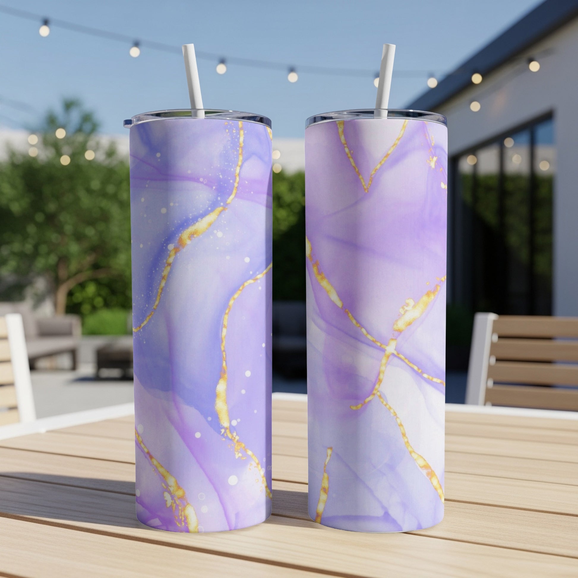 Two tall purple and gold marbled tumblers with straws on a wooden table.