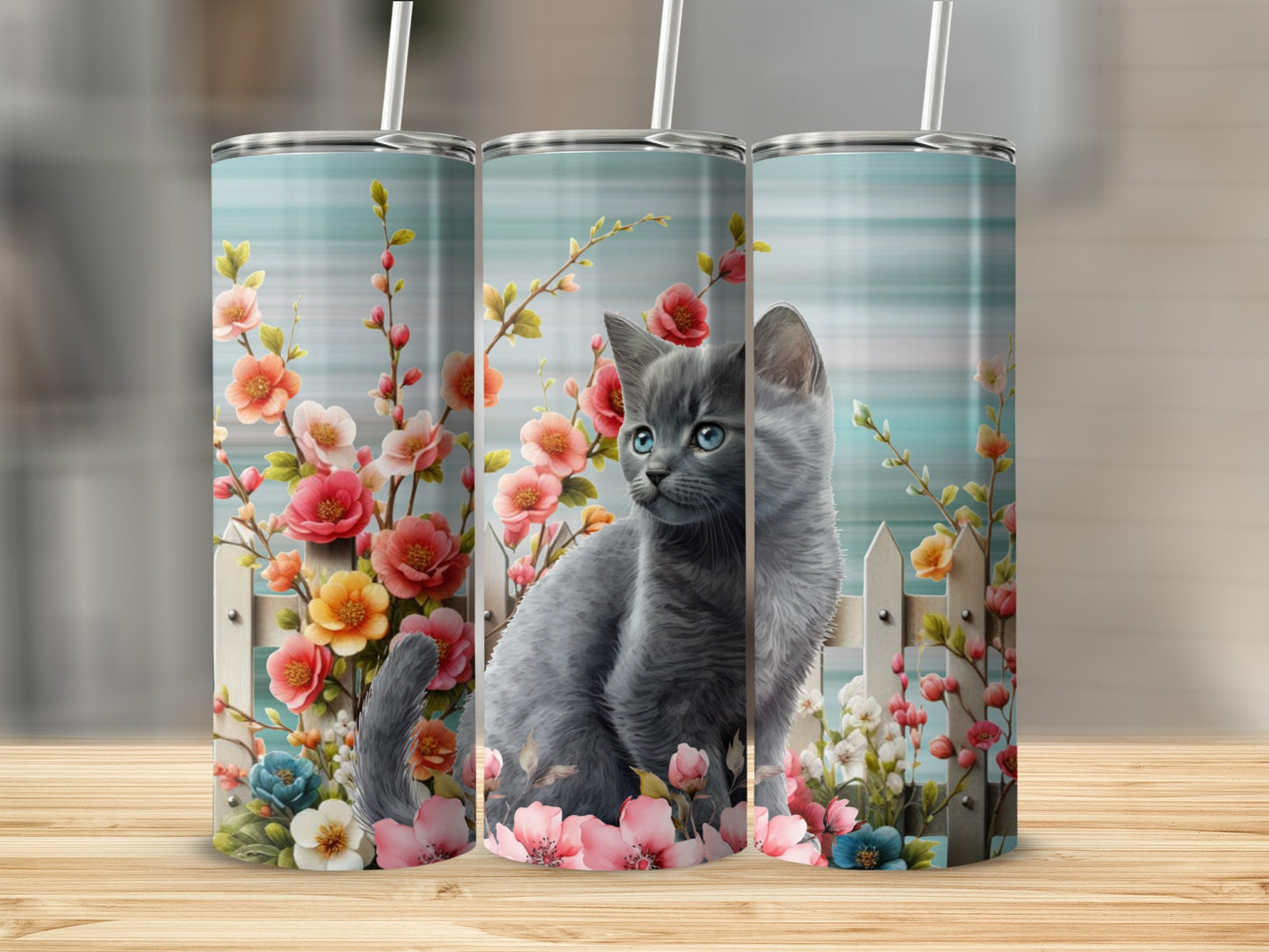Gray kitten sitting among colorful flowers and a white picket fence.