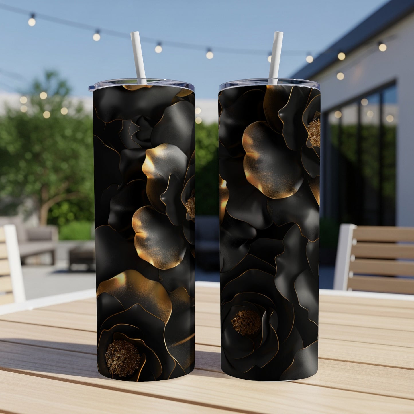 Two black tumblers with gold floral design on an outdoor table.