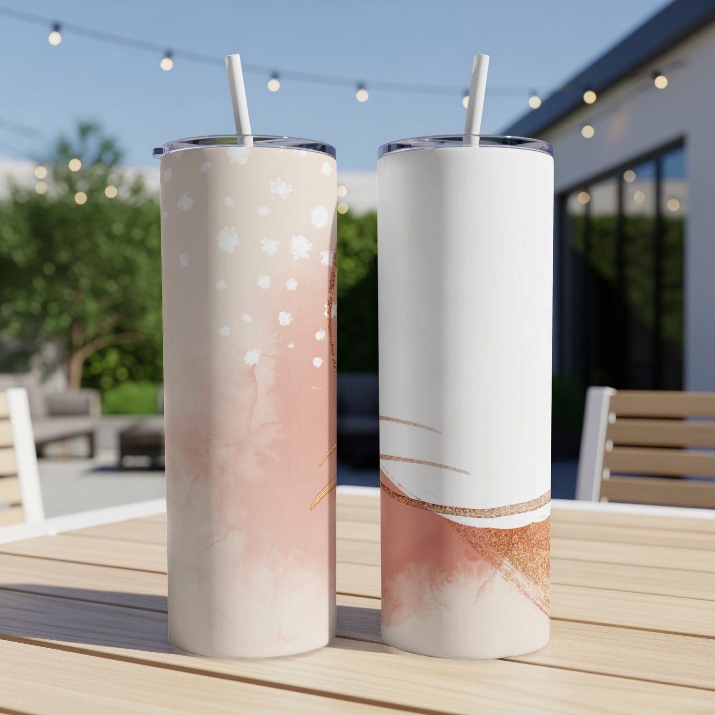 Two skinny tumblers, one with a pink and gold abstract design, sit on a wooden table.
