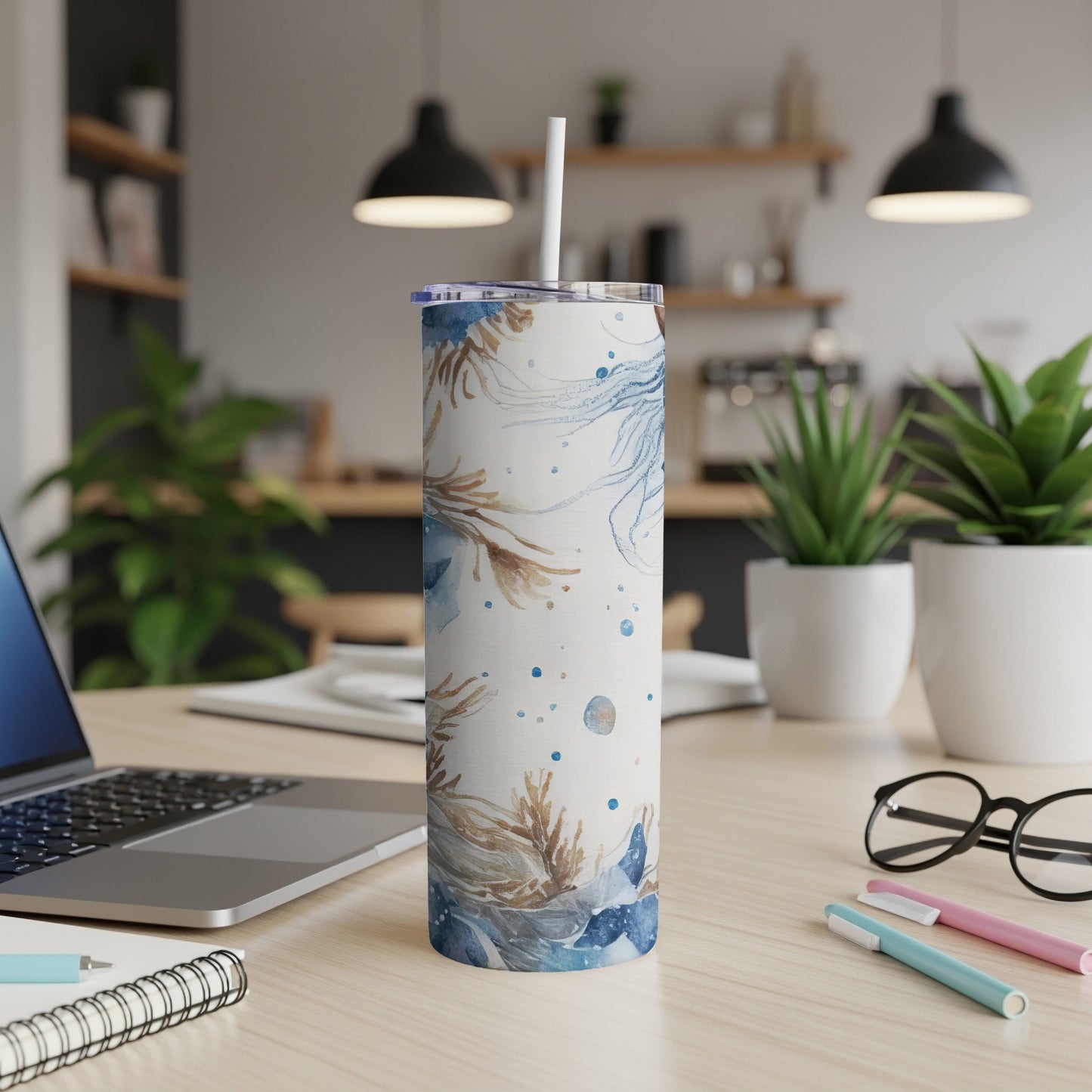 Tall tumbler with blue and brown floral design, straw, on a desk.
