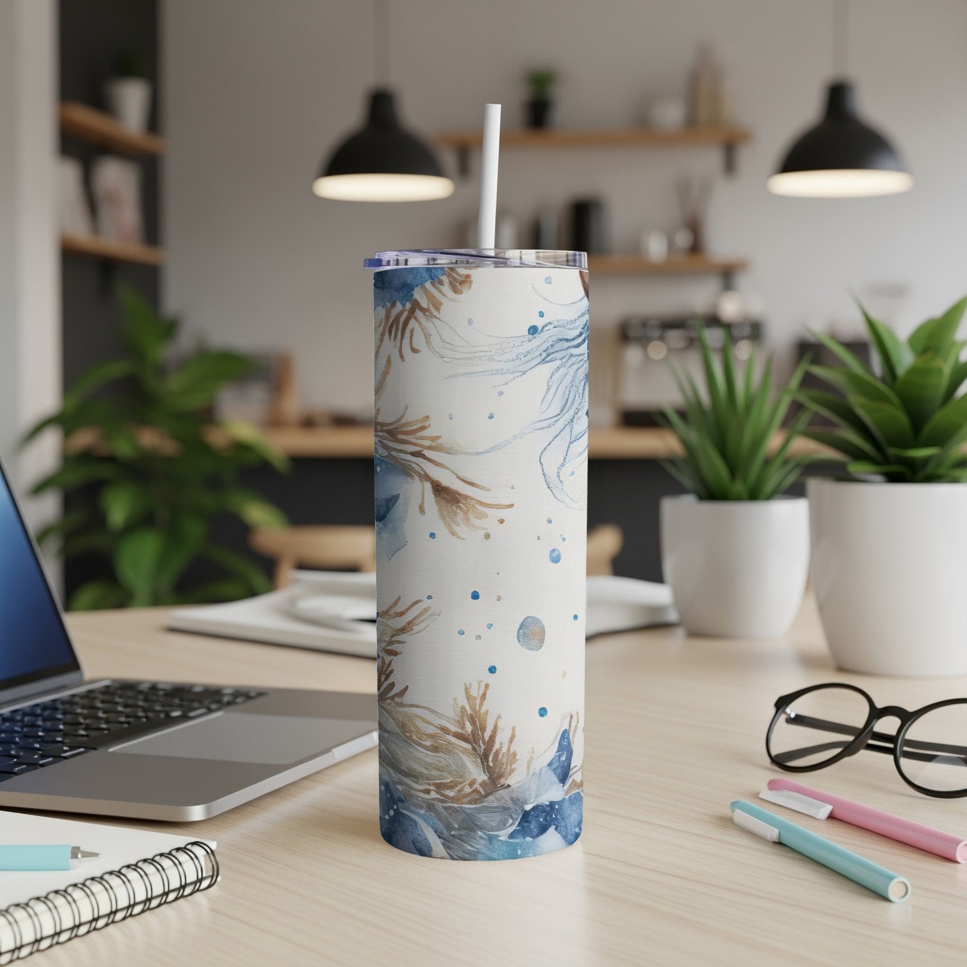 Tall tumbler with blue and brown floral design, straw, on a desk.
