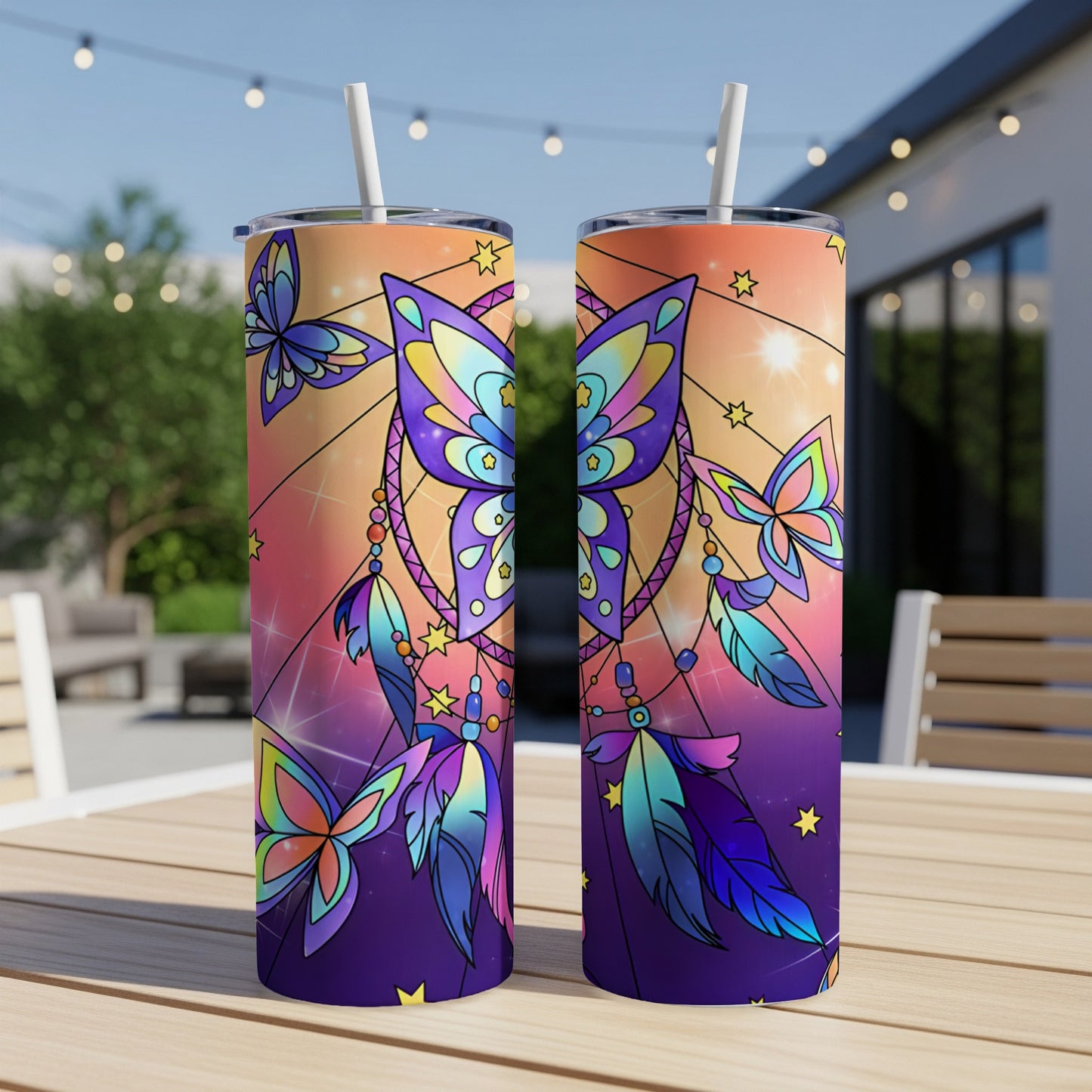 Two tall tumblers with butterfly and dreamcatcher design on outdoor table.