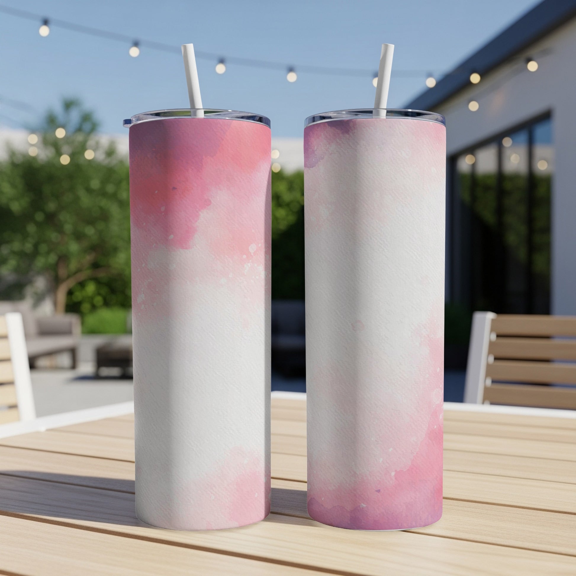 Two tall, skinny tumblers with pink watercolor designs sit on a wooden table outdoors.