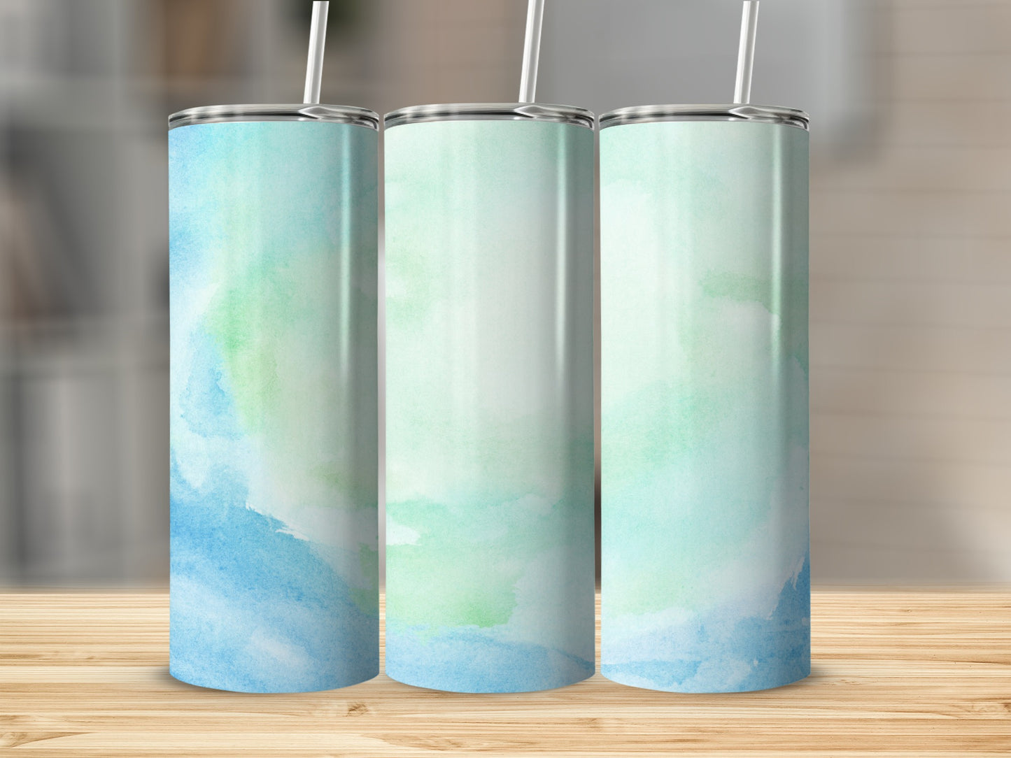 Three tall tumblers with a blue and green watercolor design on a wooden surface.