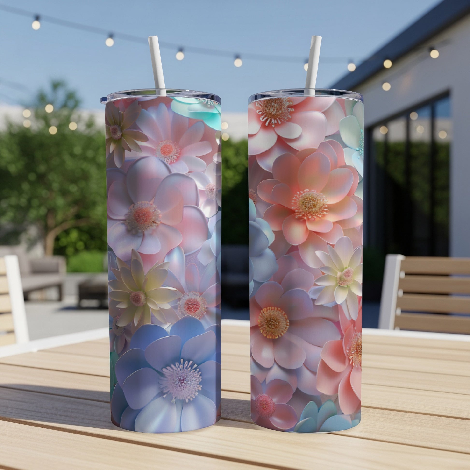 Two floral patterned tumblers with straws on a wooden table outdoors.