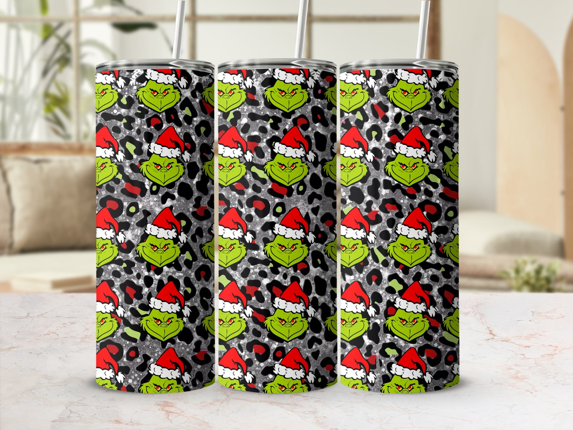 Three tumblers with a Grinch pattern on a light marble surface.