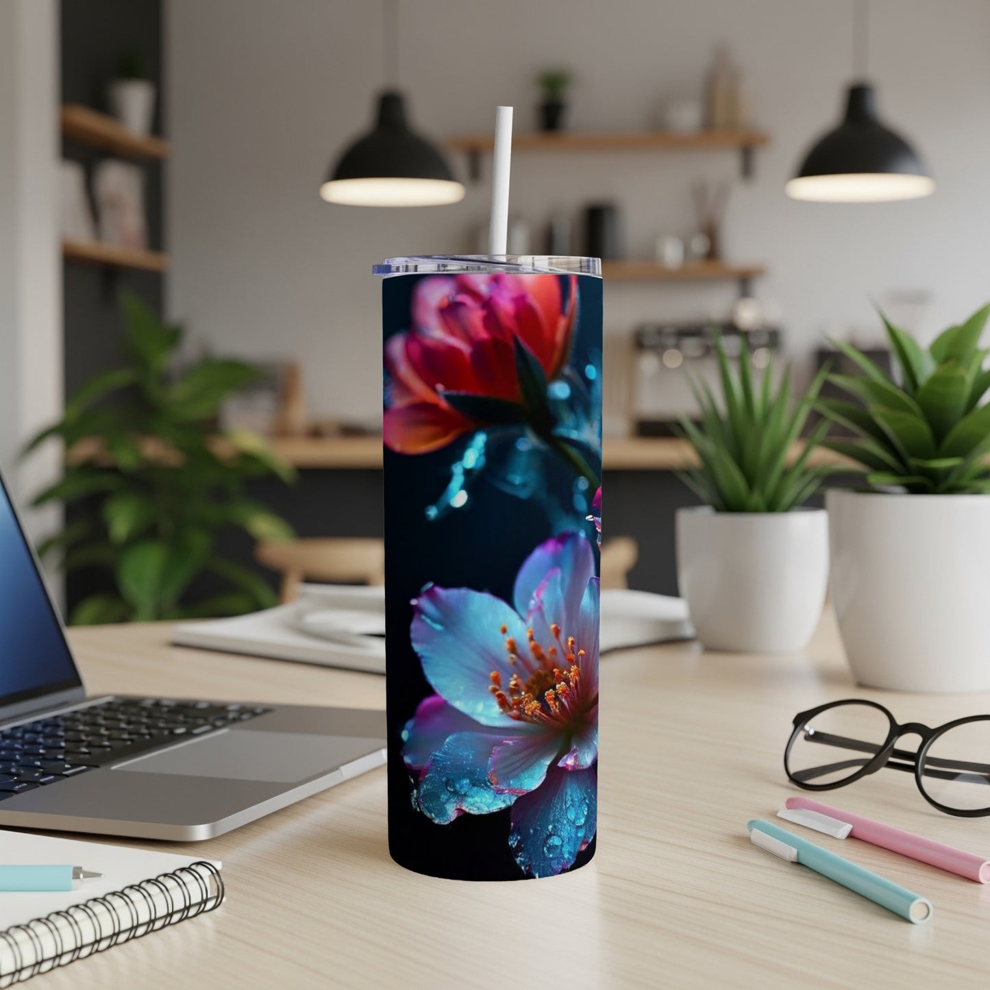 Floral pattern tumbler with a straw on a desk with a laptop and pens.