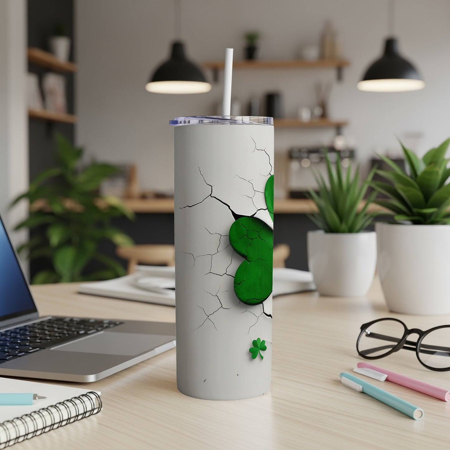 White tumbler with green shamrock design, a straw, on a desk.