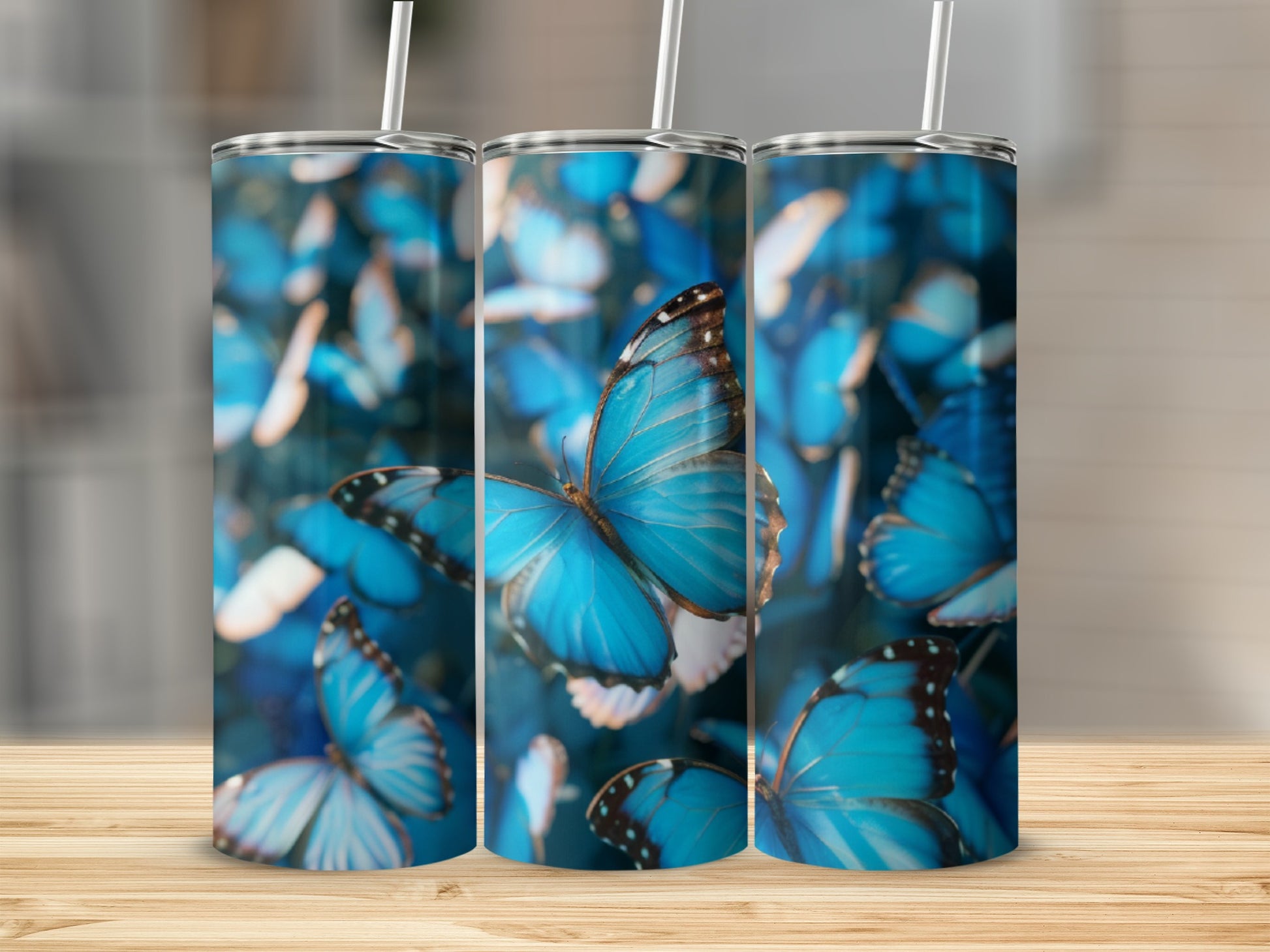 Three blue butterfly patterned tumblers with straws on a wooden surface.