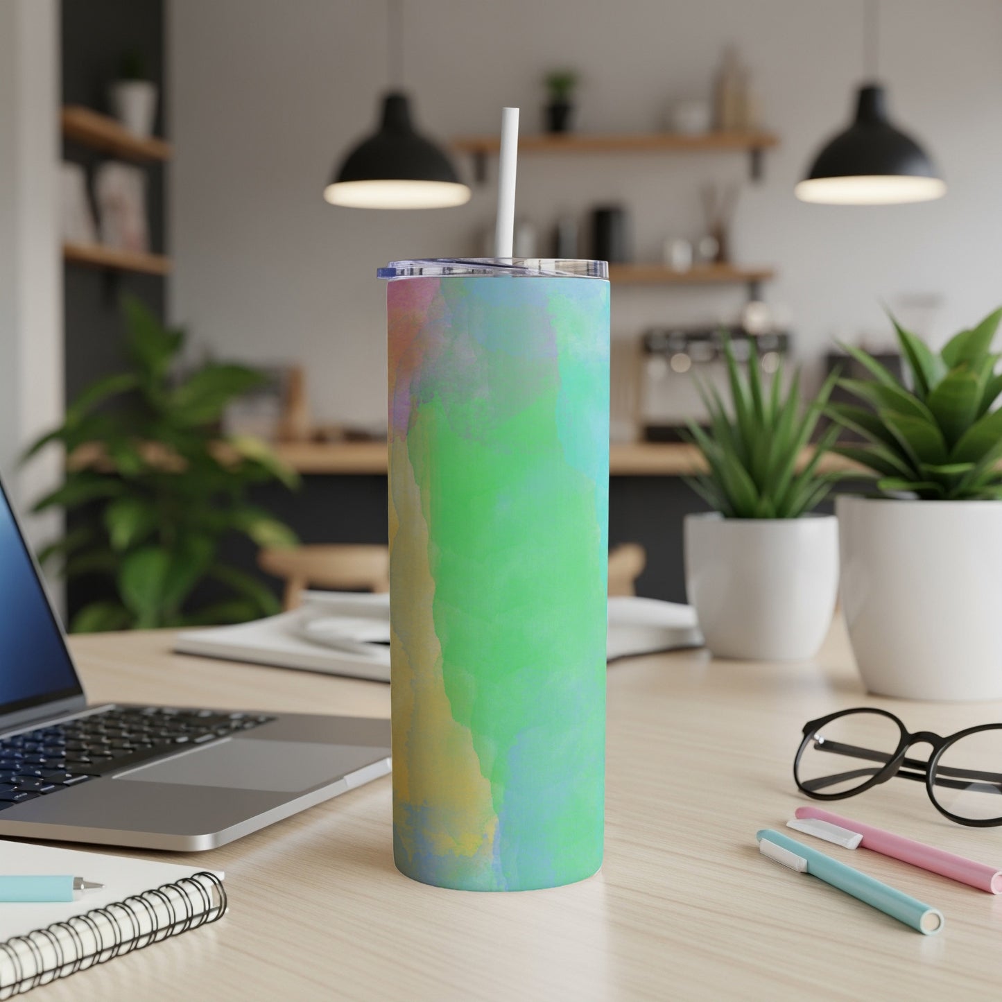 Colorful abstract tumbler with straw on a desk with a laptop.