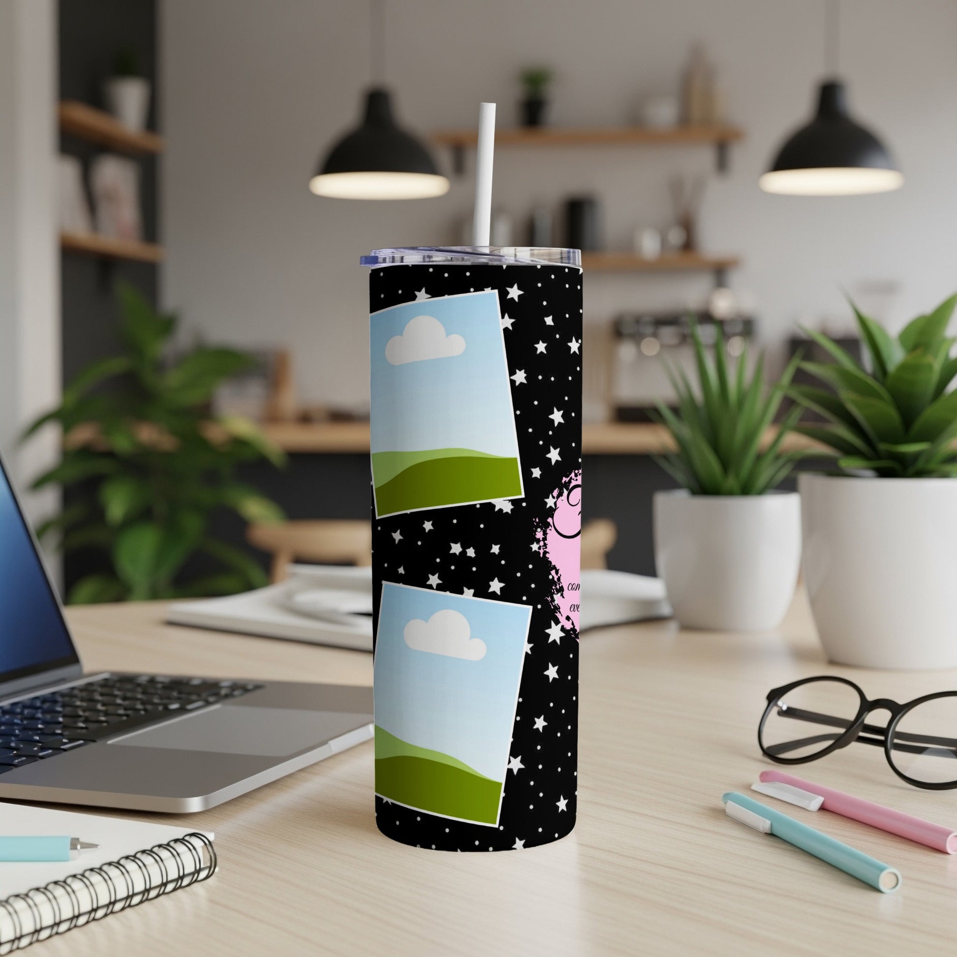 Black tumbler with stars, clouds, and pink text on a desk.