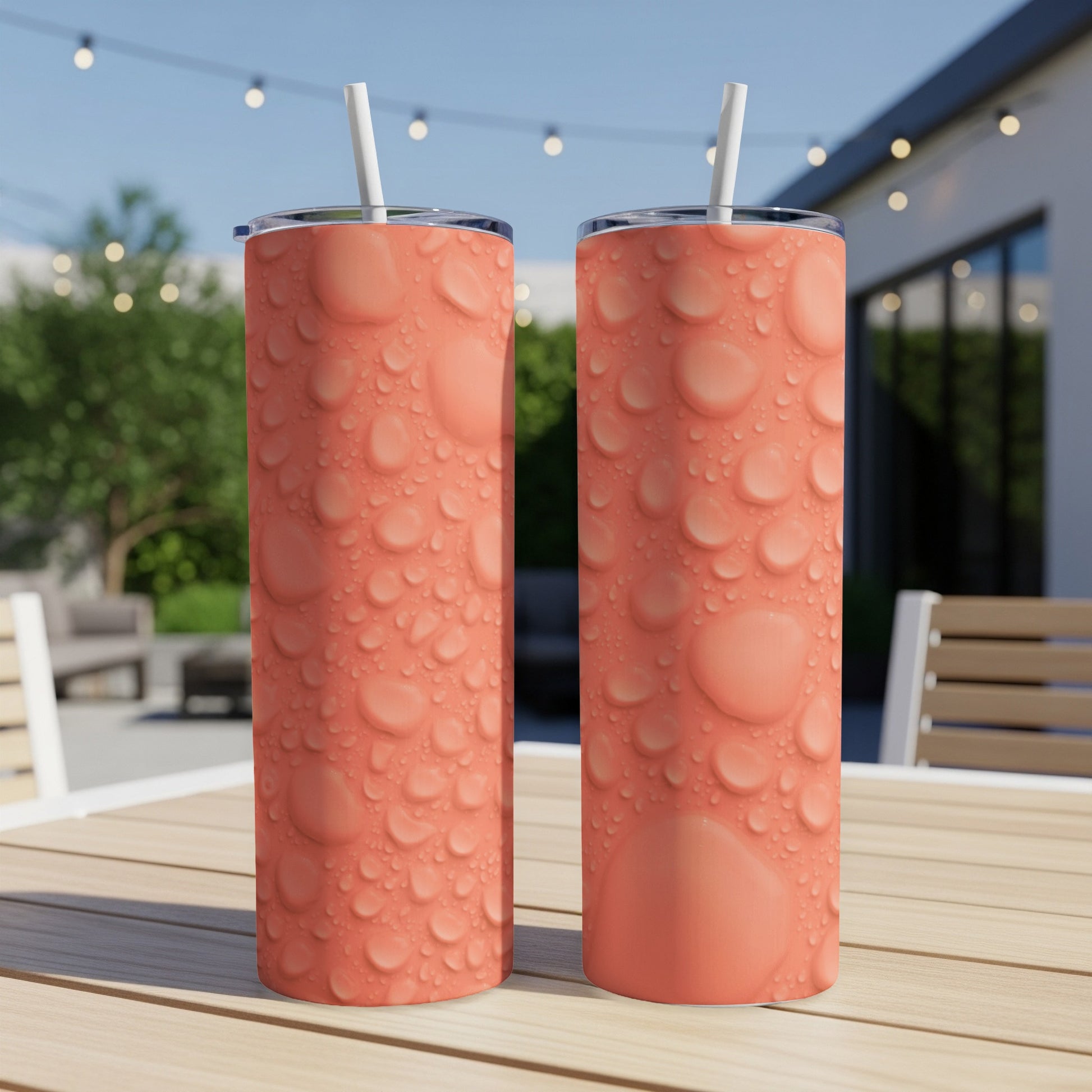 Two coral-colored tumblers with a water droplet pattern on a patio table.