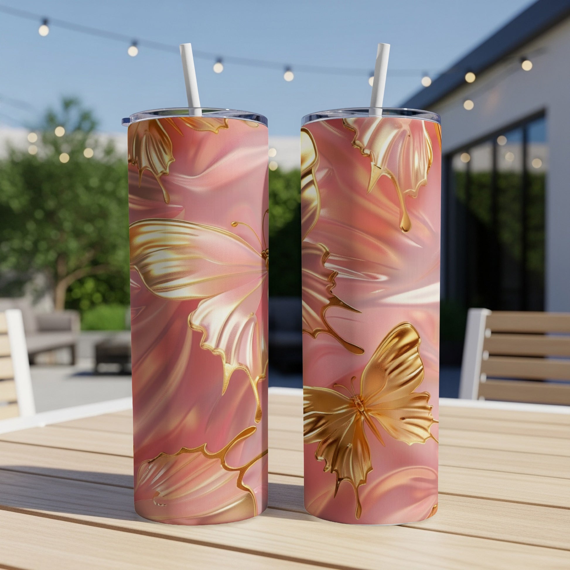 Two pink tumblers with gold butterfly designs and straws sit on a table.