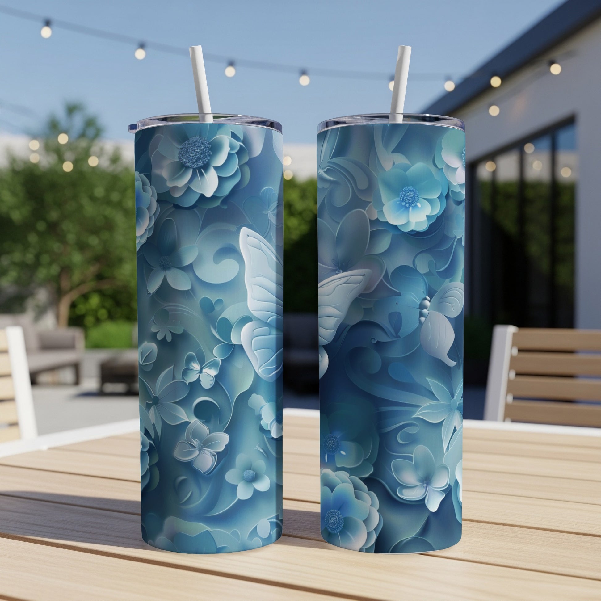 Blue floral and butterfly patterned tumblers with straws on a wooden table.