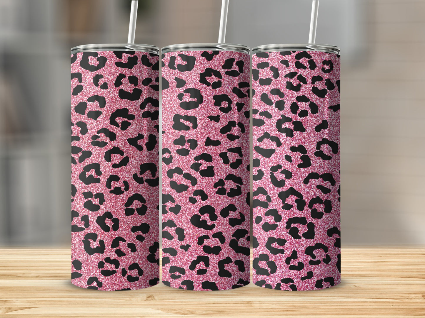 Three pink glitter leopard print tumblers with straws on a wooden surface.