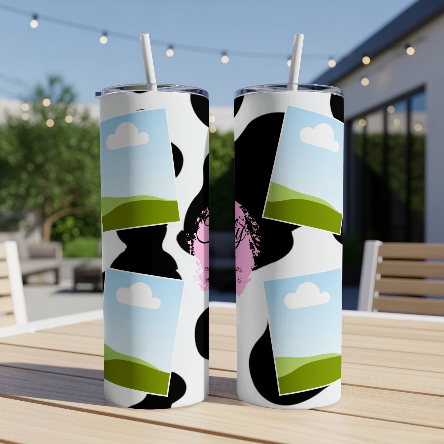 Two cow print tumblers with sky and landscape inserts sit on a wooden table.