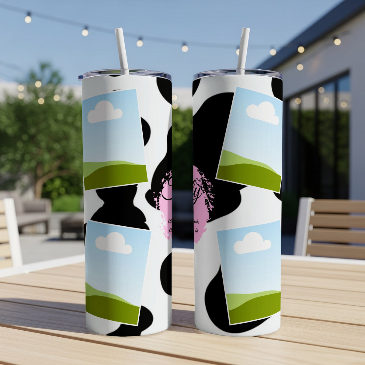 Two cow print tumblers with sky and landscape inserts sit on a wooden table.