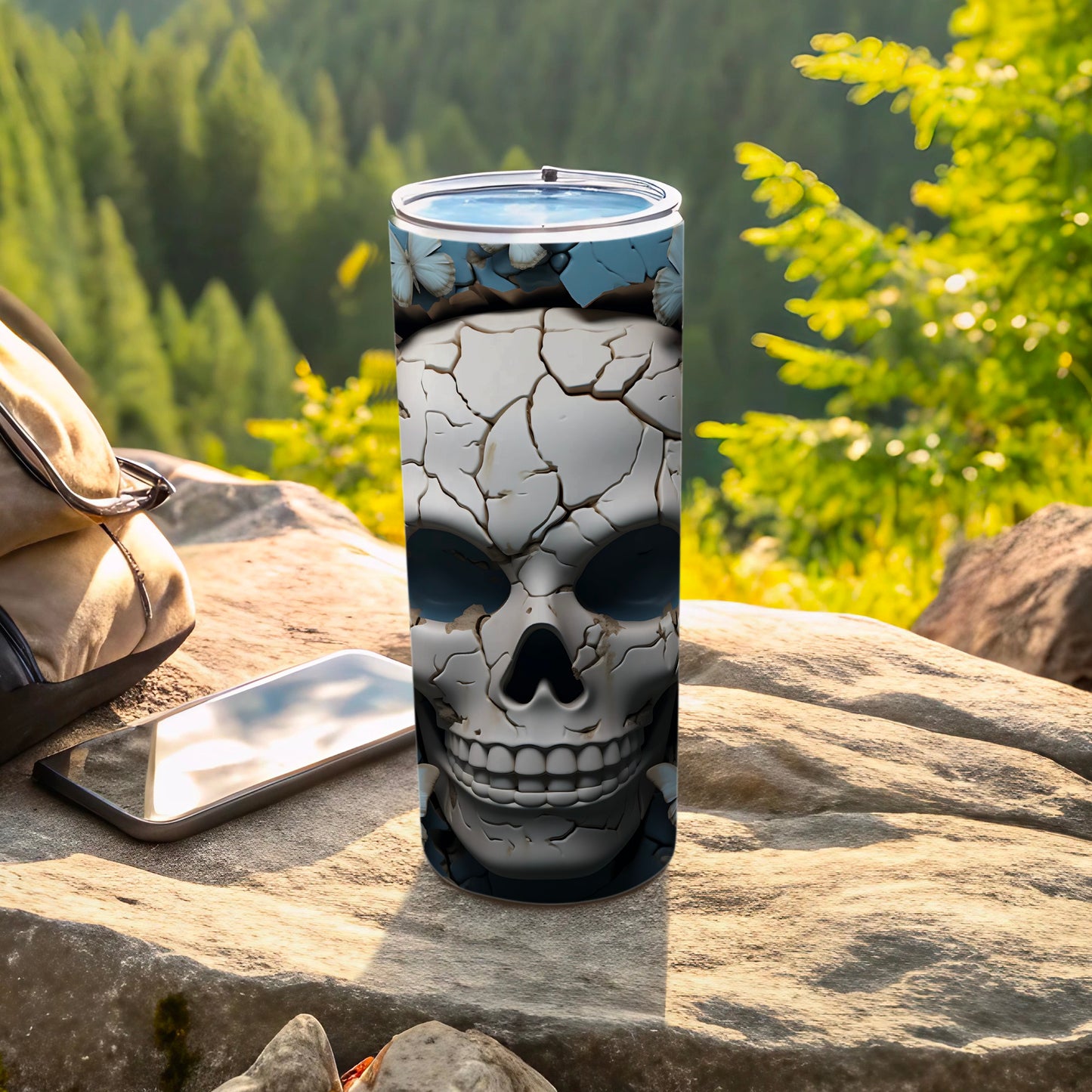 Cracked skull tumbler next to backpack and phone on rock outdoors.
