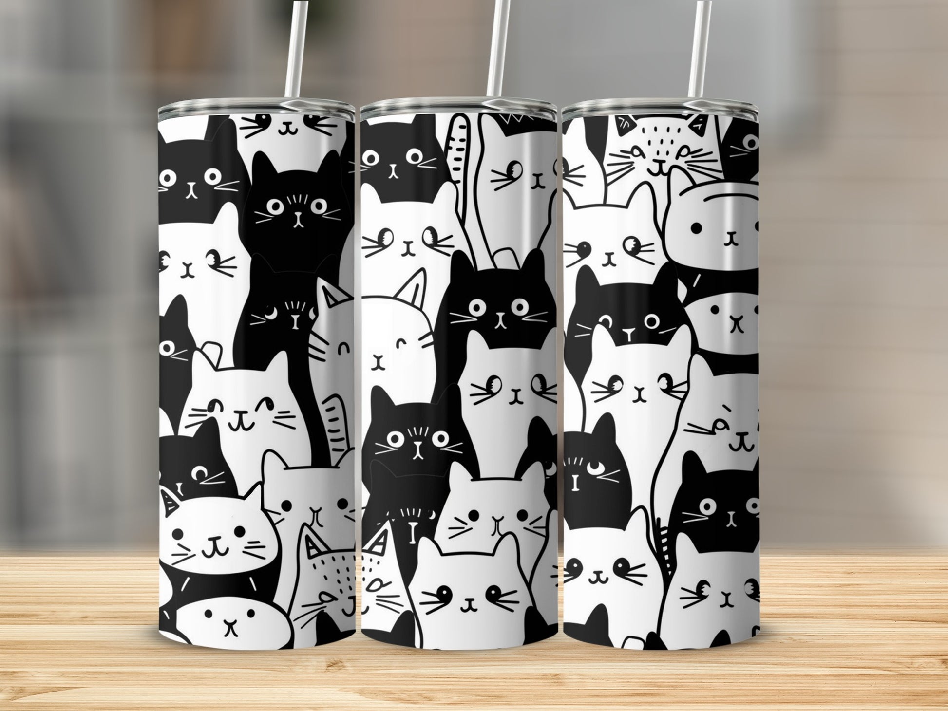Three black and white cat patterned tumblers with straws on a wooden surface.