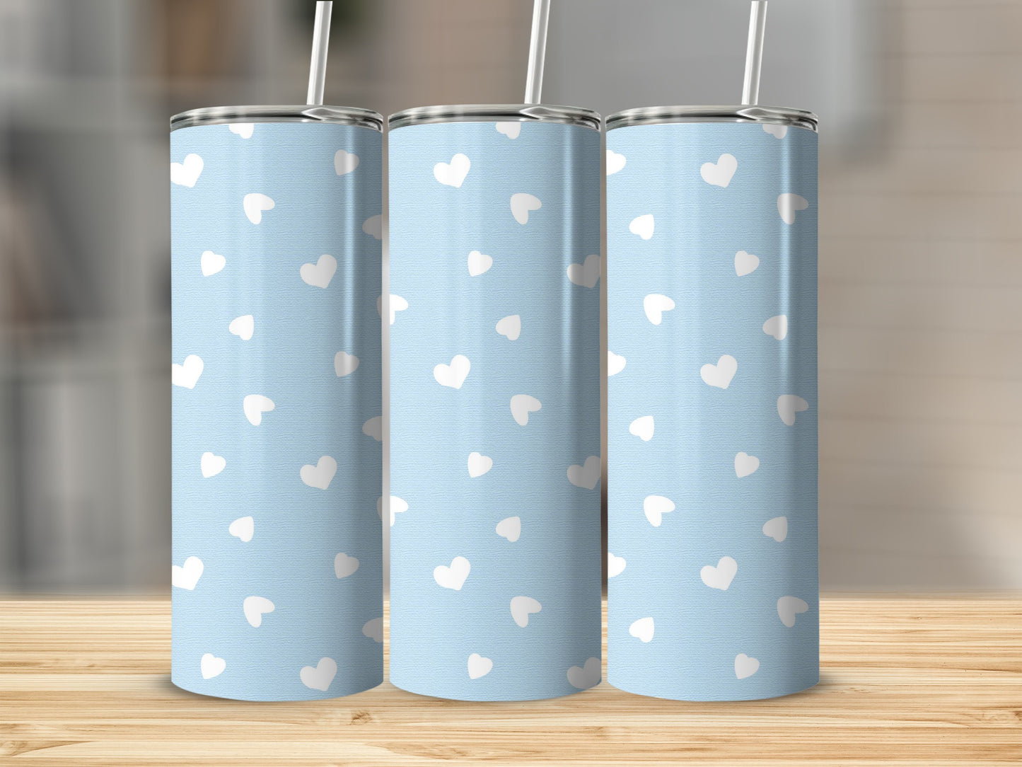 Three tall, light blue tumblers with a repeating white heart pattern and straws.